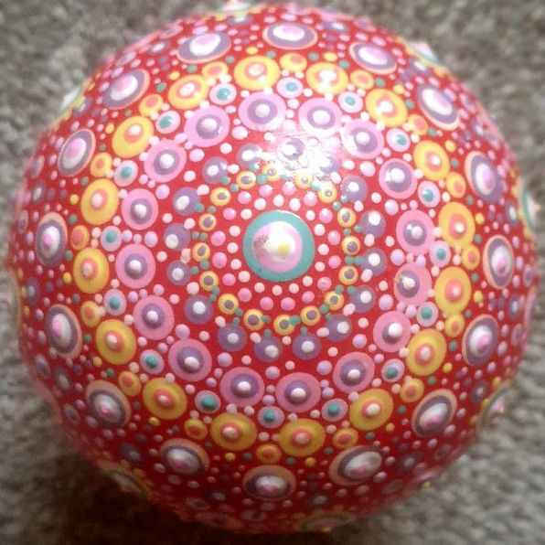 A vibrant mandala pattern on a spherical object, featuring concentric circles in pink, yellow, and blue against a red background, conveying a playful tone.