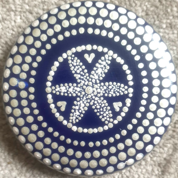 Round blue object with a central dotted flower pattern, surrounded by heart shapes and concentric dot circles, creating a decorative, calming design.
