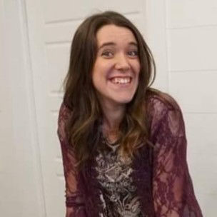 An image of Jasmine as she smiles warmly at the camera. She is wearing a lace-patterned purple top. The background features a white, paneled door.