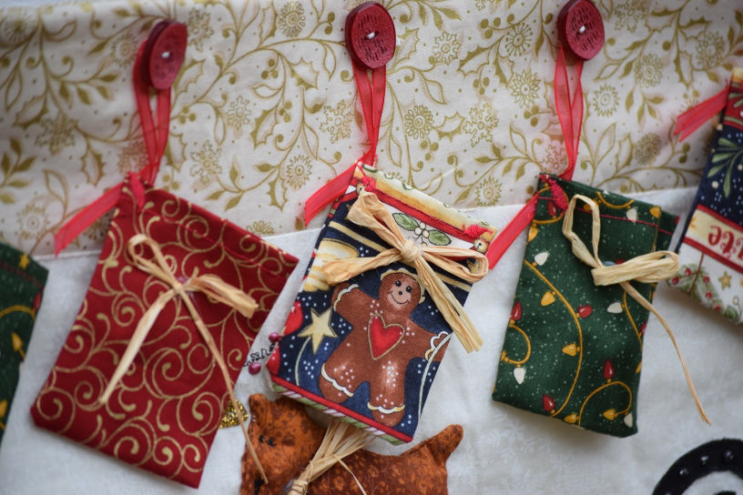Close-up of festive fabric gift bags hanging in a row, each tied with raffia on bright red ribbons. The middle pouch features a gingerbread man.