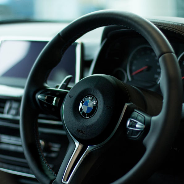 Close-up of a steering wheel. In the background, car dashboard and infotainment screen are slightly blurred.